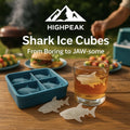 HighPeak Shark Ice Cube Mold in blue silicone with shark-shaped ice cubes and a whiskey glass on a wooden table outdoors