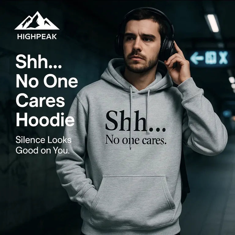 HighPeak Shh No One Cares Hoodie in gray with bold text, worn by man with headphones in dim urban setting