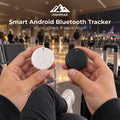 A person in an airport holding two small round Bluetooth trackers, one white and one black, with text overlay reading 'HIGHPEAK Smart Android Bluetooth Tracker' at the top.