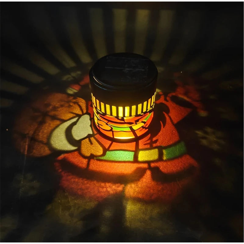 Close-up of the illuminated cylindrical Solar Santa Projection Light casting colorful Santa patterns around its base