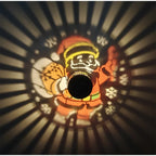 Black Solar Santa Projection Light surrounded by radial beams and colorful Christmas patterns