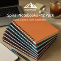HighPeak Spiral Notebooks - 12 Pack with hardcovers in jewel tones stacked on a desk beside a laptop and pen