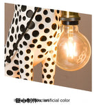 Close-up of the Spotted Cheetah Premium Lamp glowing globe bulb, gold-tone holder and white body with black spots.