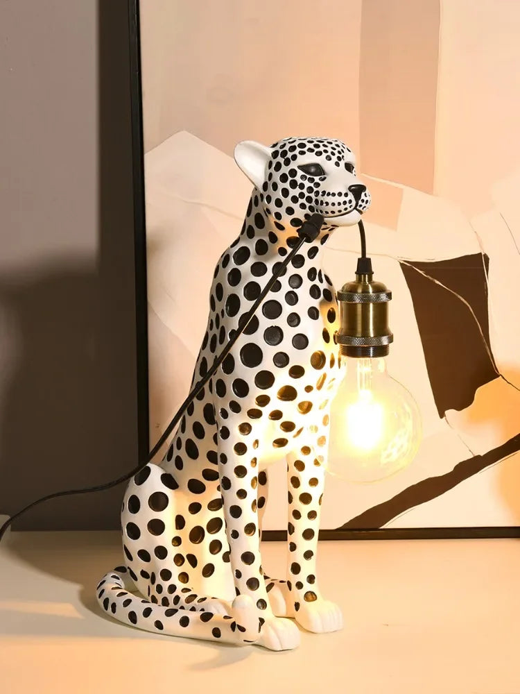 White Spotted Cheetah Premium Lamp holding a glowing bulb by the cord in front of a black-and-white abstract print.