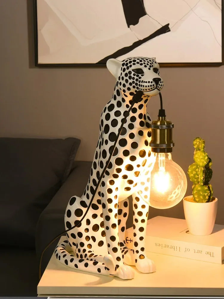 White Spotted Cheetah Premium Lamp holding a lit globe bulb by its cord on a side table beside a cactus and books.