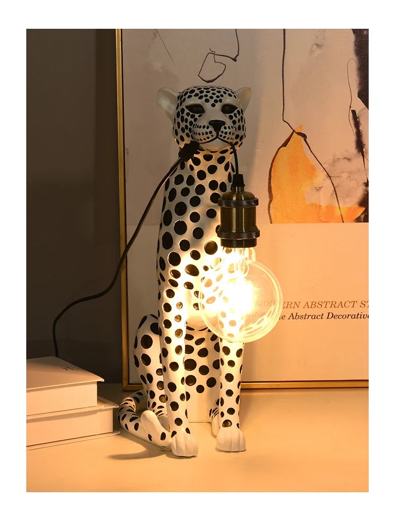 White Spotted Cheetah Premium Lamp viewed from the front with a glowing hanging bulb, books and framed artwork.