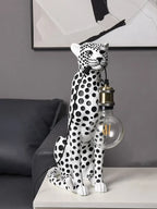 Front view of the white Spotted Cheetah Premium Lamp with black spots and an unlit clear globe bulb beside a gray sofa.