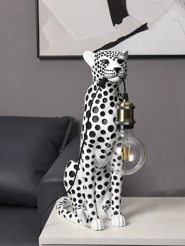 Front view of the white Spotted Cheetah Premium Lamp with black spots and an unlit clear globe bulb beside a gray sofa.