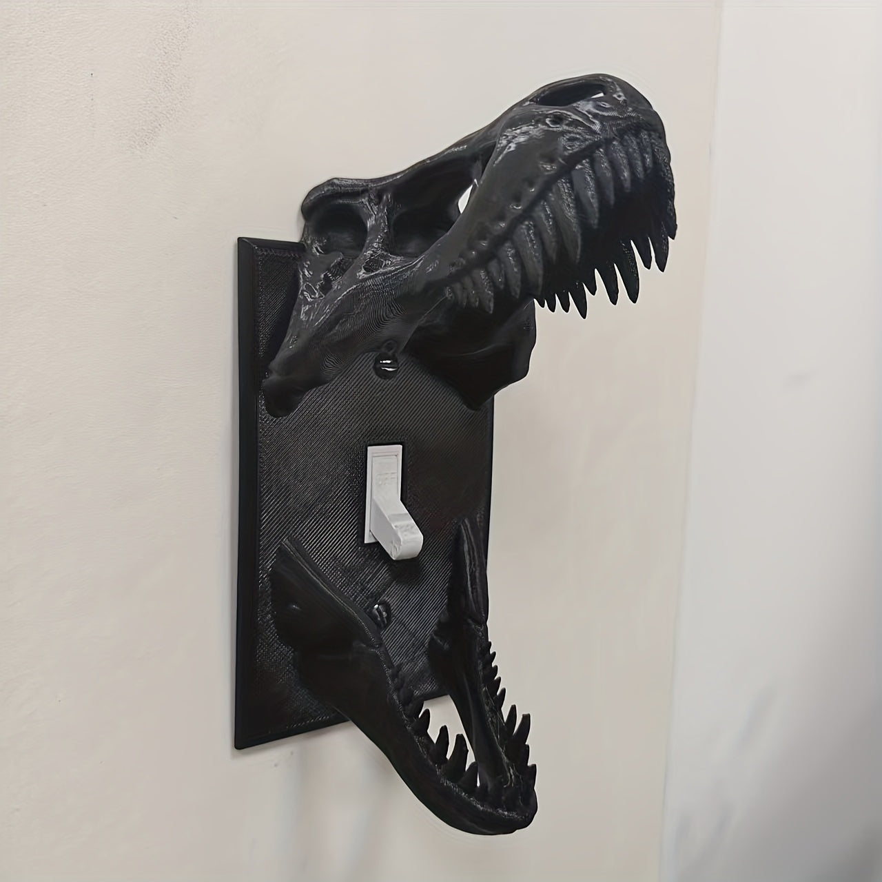 Black T-Rex Skull Switch Cover viewed from the opposite side on a light wall