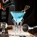 Jellyfish Cocktail Glass with a blue cocktail and olive garnish, showing the clear tentacles during pouring.