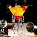 Jellyfish Cocktail Glass with a layered orange and red drink, ice, and a cherry beside a metal jigger.