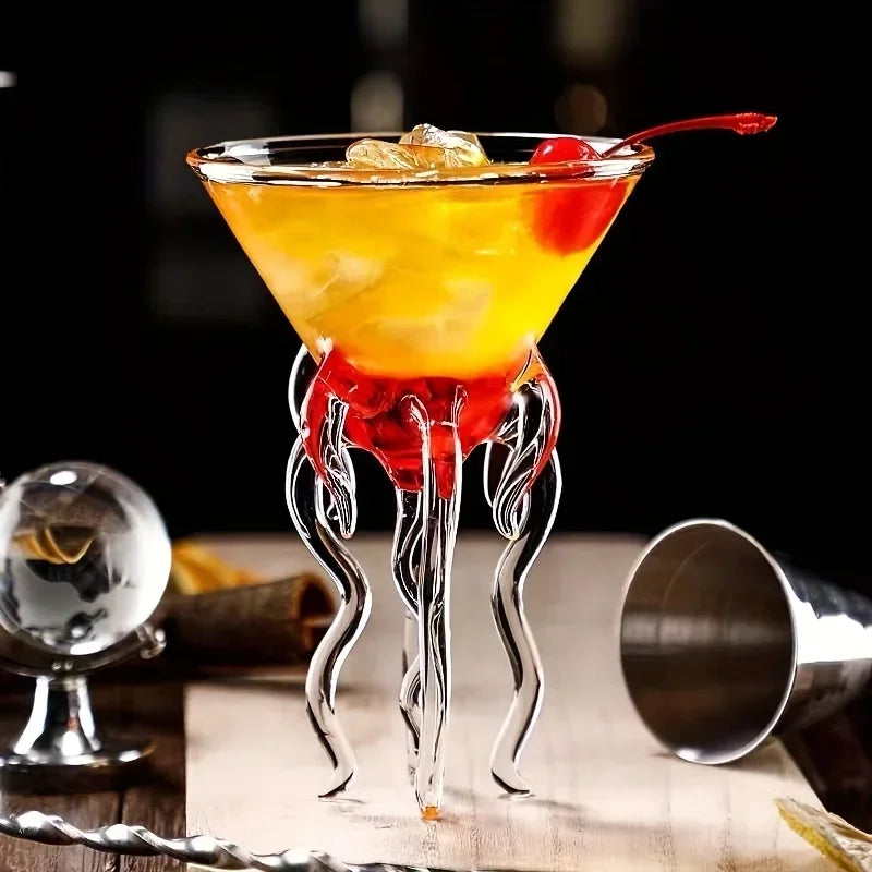 Jellyfish Cocktail Glass with a layered orange and red drink, ice, and a cherry beside a metal jigger.