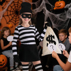 Child in a striped burglar outfit with a money bag at an indoor Halloween party with question-mark cards.