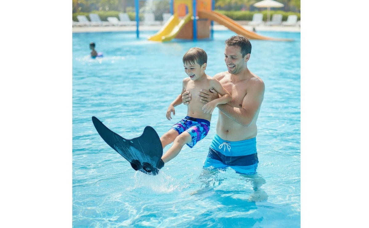 Kids Mermaid Swim Fin in a wide pool scene showing an adult holding a child wearing the black monofin.