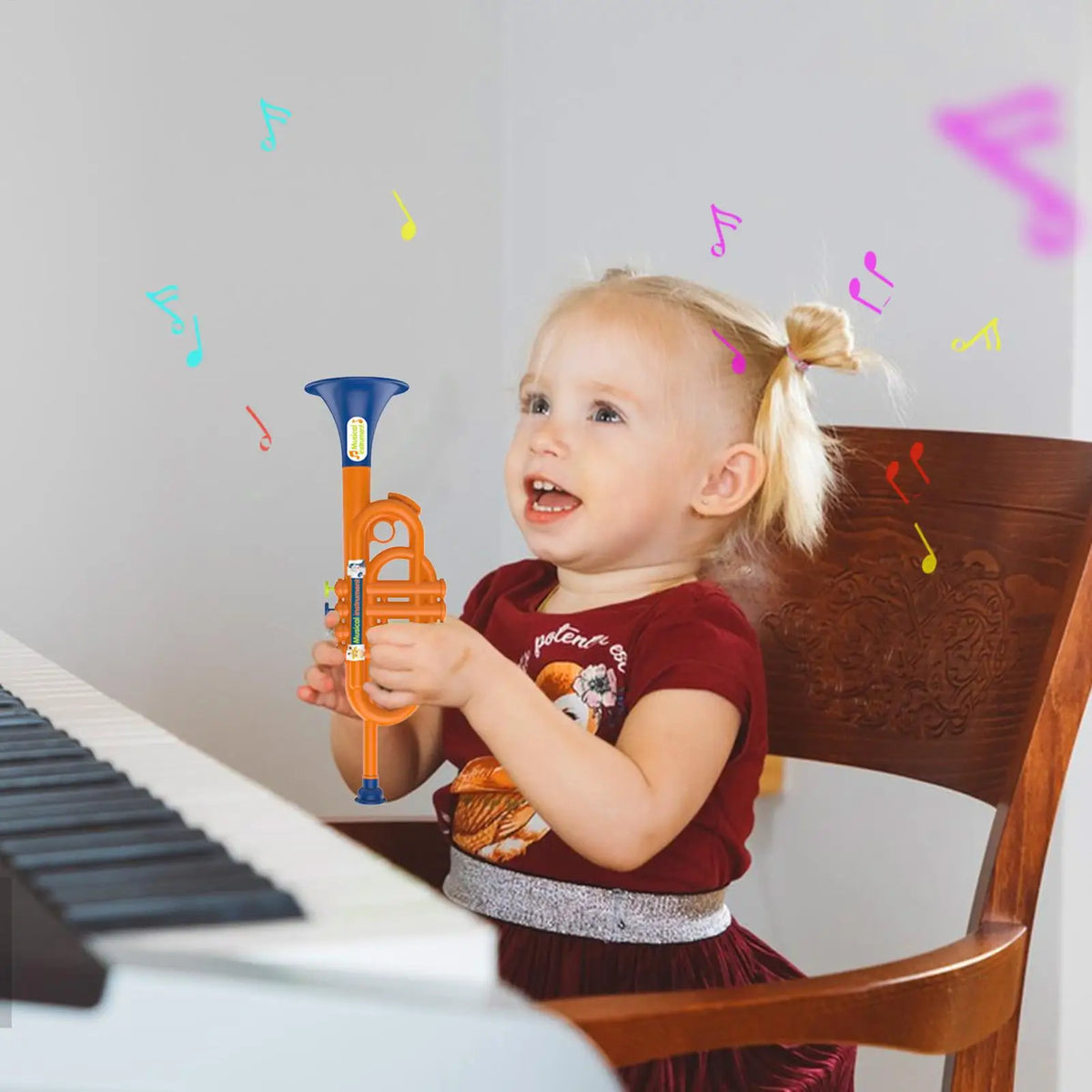 Kids Musical Toy Trumpet girl holding the orange and blue toy beside a piano