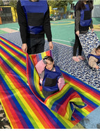 Kids Rainbow Pull Game Mat with a seated child and an adult holding the raised fabric during playground play