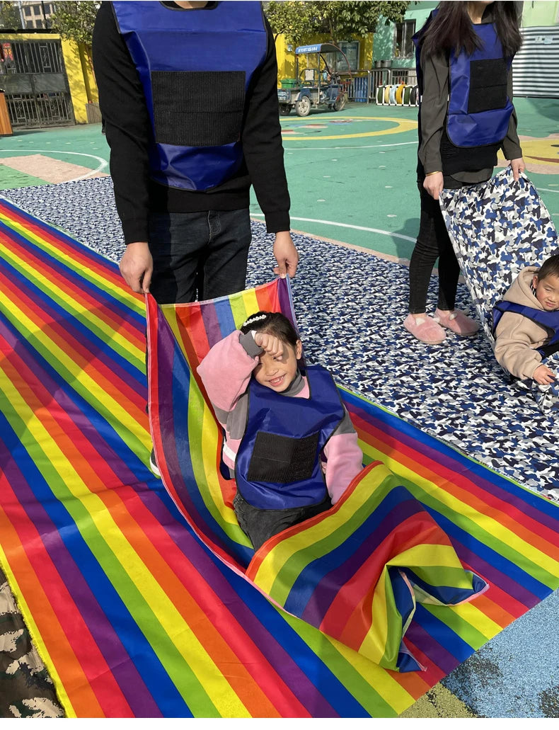 Kids Rainbow Pull Game Mat with a seated child and an adult holding the raised fabric during playground play