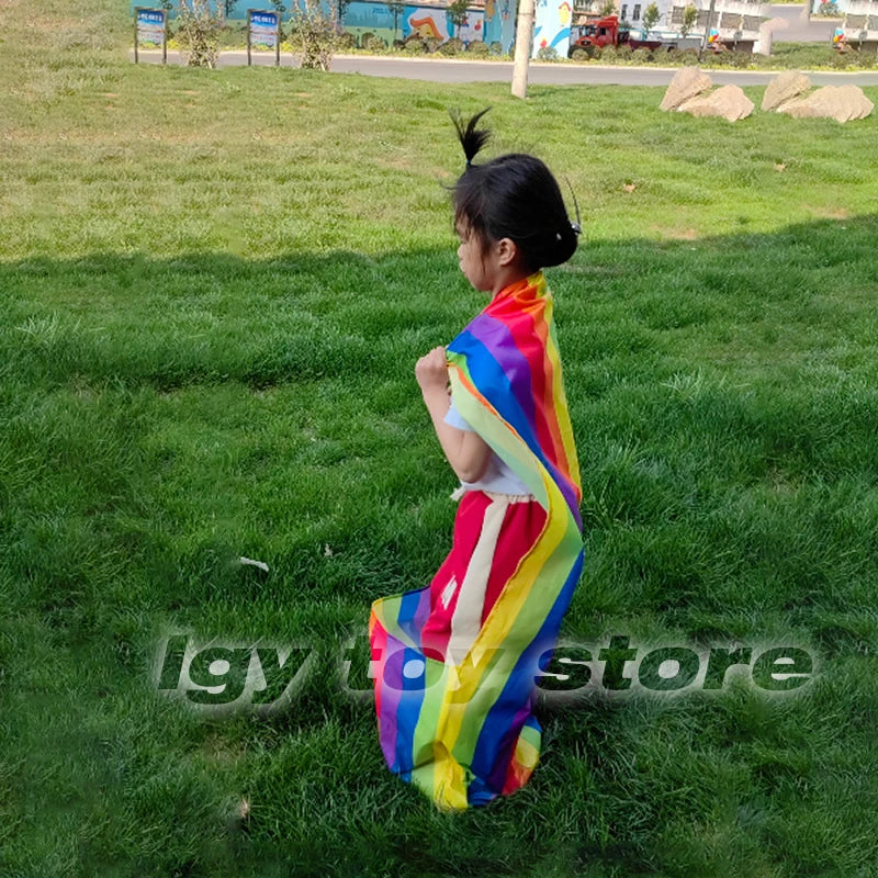 Kids Rainbow Pull Game Mat with rainbow fabric gathered around a standing child during outdoor pocket play