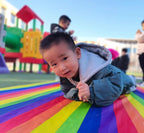 Kids Rainbow Pull Game Mat with a child lying on the rainbow-striped fabric at a playground