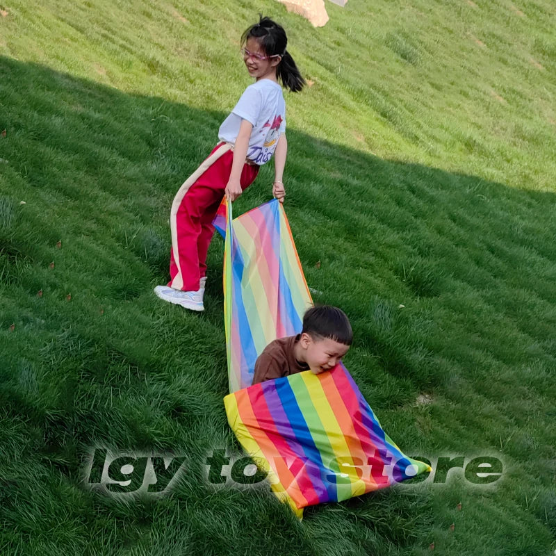 Kids Rainbow Pull Game Mat stretched between a seated boy in the pocket and a girl holding the fabric on grass