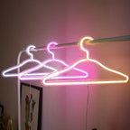 LED Glowing Clothes Hanger outlines in white, pink and warm white hanging from a clothing rail