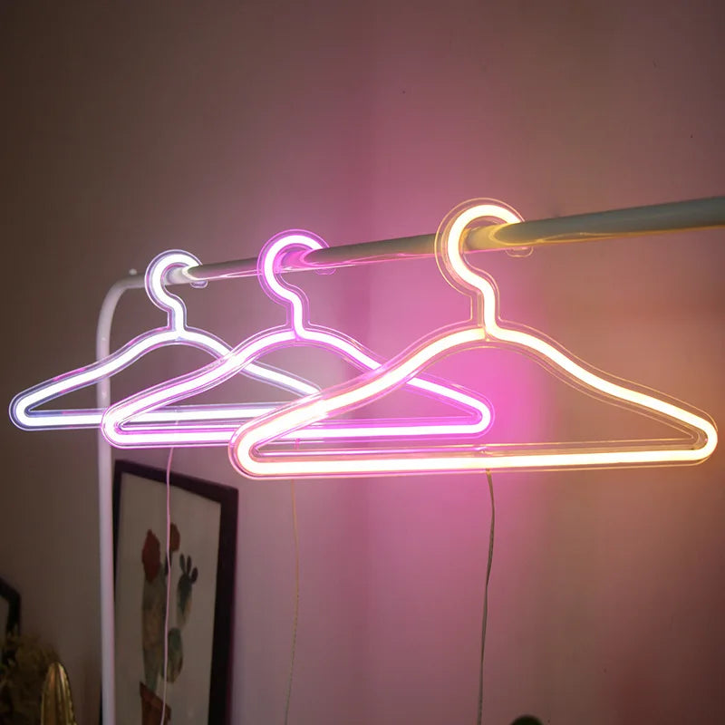 LED Glowing Clothes Hanger outlines in white, pink and warm white hanging from a clothing rail