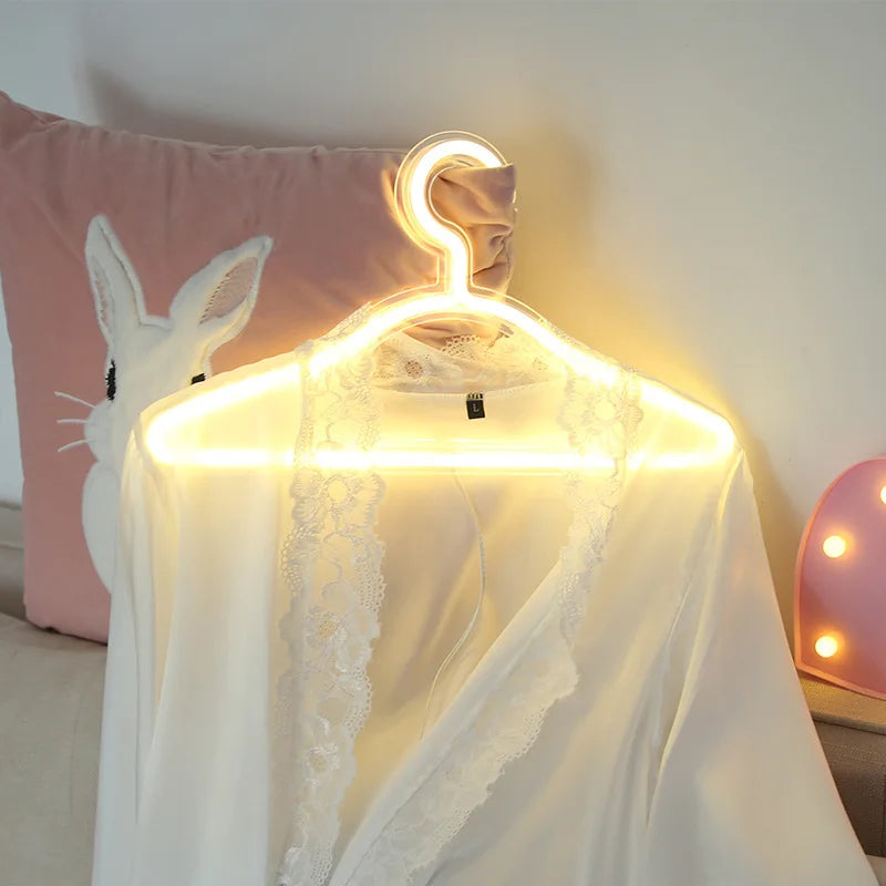 LED Glowing Clothes Hanger in warm white illuminating a white lace-trimmed robe beside a pink cushion