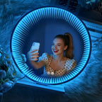 Ice-blue LED Infinity Tunnel Mirror reflecting a woman taking a selfie, with glowing rings on a white stand.