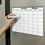 Magnetic Fridge Calendar on a silver fridge with a hand holding a dry erase marker over the monthly grid.