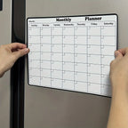 Magnetic Fridge Calendar with a white monthly grid being positioned on a silver refrigerator door.