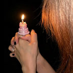 Mini Birthday Cake Ring in pink worn on a hand, with a lit candle against a dark party background.