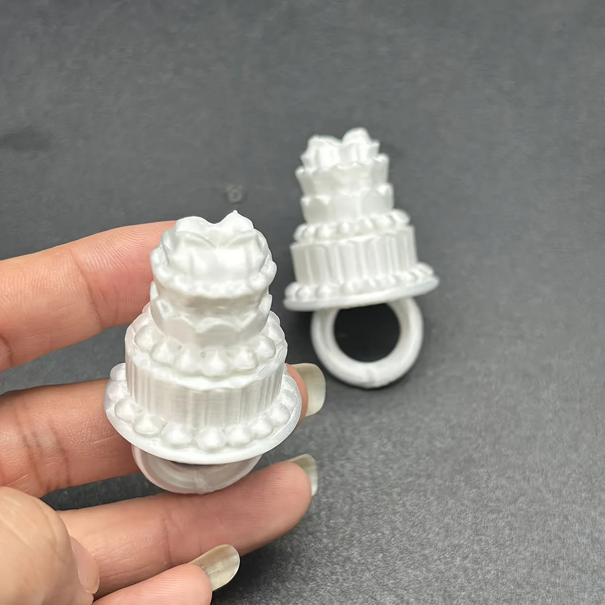 Mini Birthday Cake Ring white design held in front of a second ring, showing sculpted cake details.