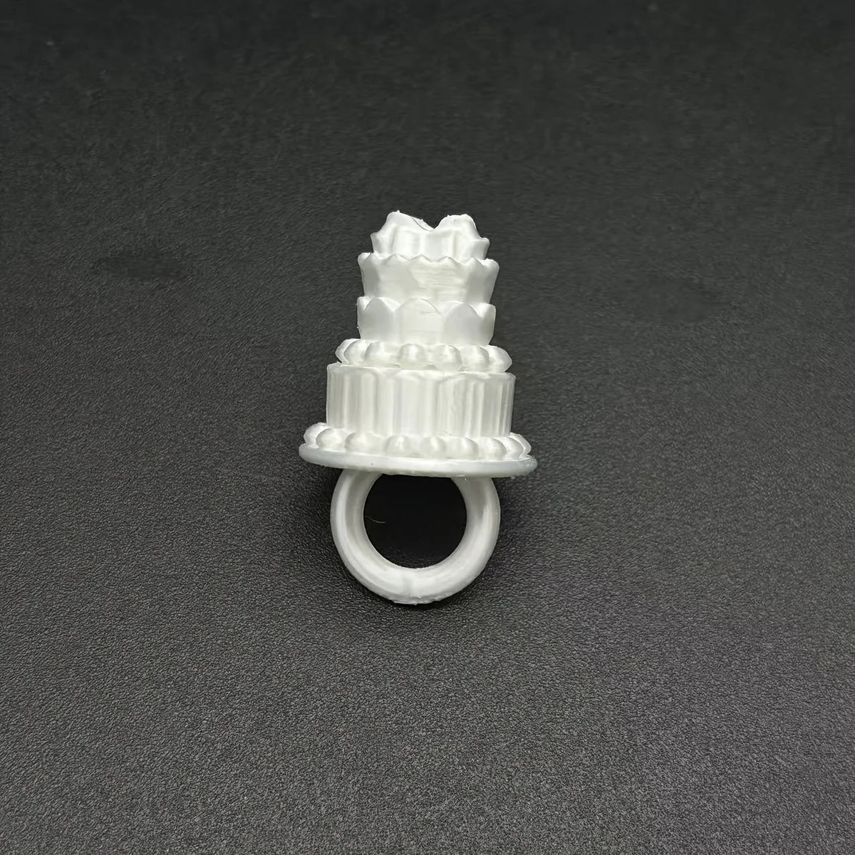 Mini Birthday Cake Ring in white viewed from the front on a dark surface, with the circular band visible.