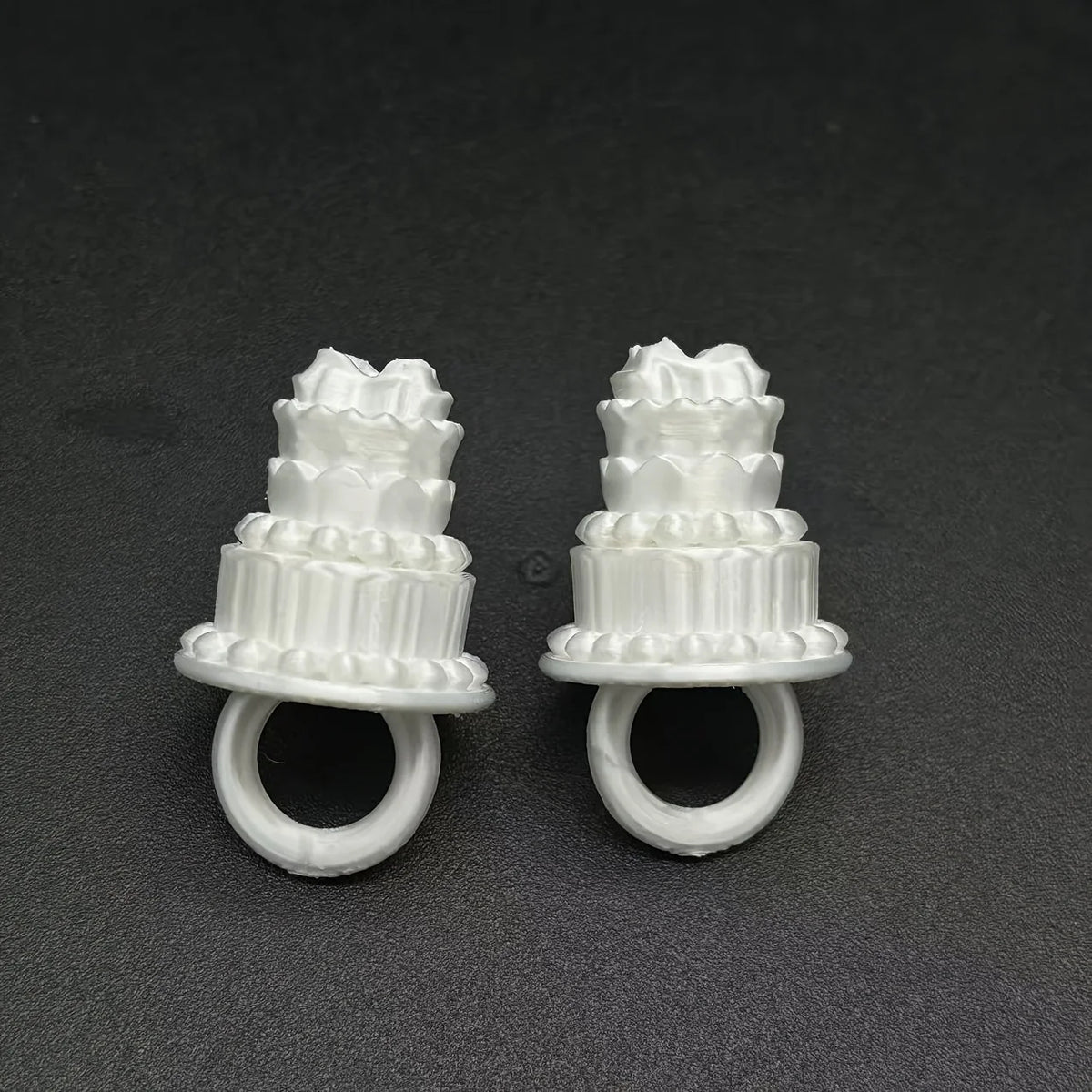 Mini Birthday Cake Ring in white shown as two examples side by side on a dark textured surface.