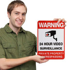 No Trespassing Security Sign held by a man, showing red warning lettering and a black surveillance camera graphic.