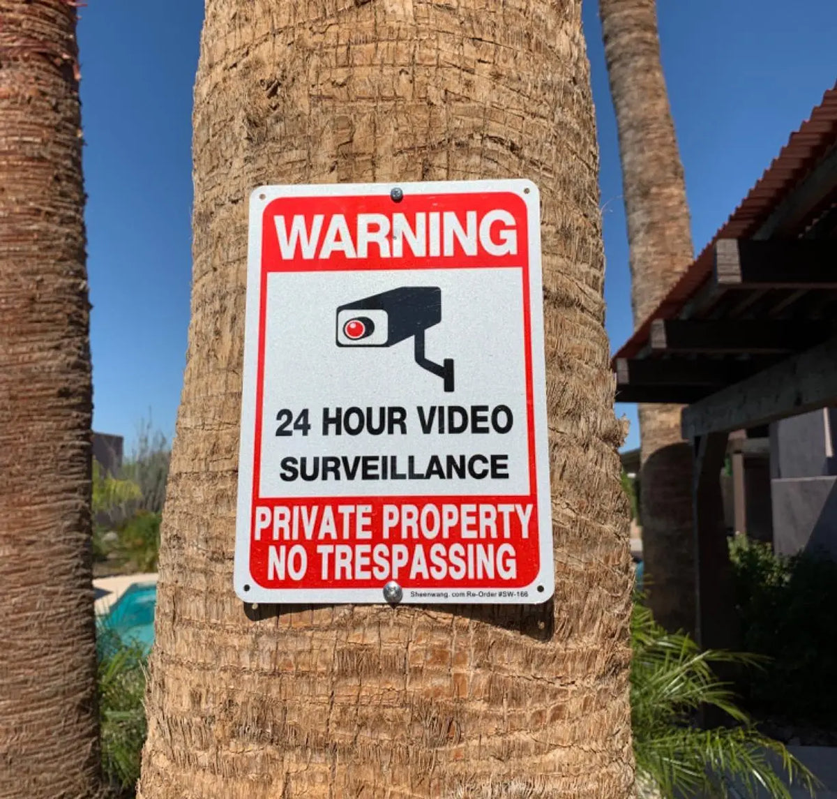 No Trespassing Security Sign attached to a palm tree near a property with a pool.