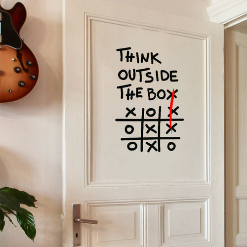Outside The Box Decal on a white paneled door beside a wall-mounted guitar and green houseplant
