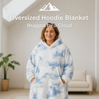 HighPeak Oversized Hoodie Blanket in blue and white cloud pattern worn by a smiling woman in a cozy living room