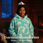 HighPeak Oversized Hoodie Blanket in teal cloud pattern with sherpa lining worn by woman indoors by fireplace