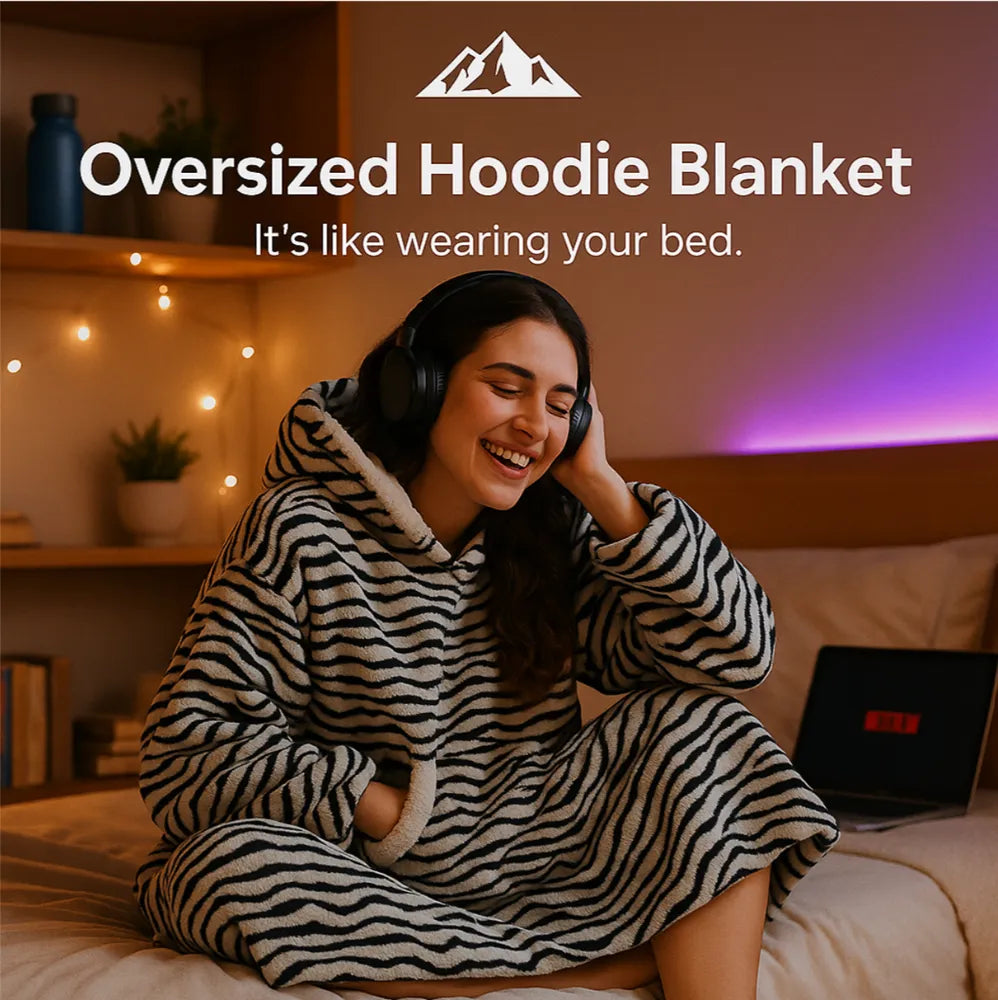 HighPeak Oversized Hoodie Blanket in zebra print worn by smiling woman with headphones on bed in cozy room