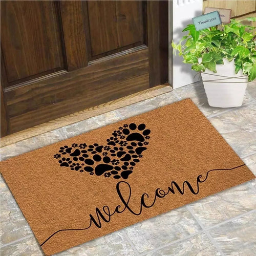 Paw Heart Welcome Mat in brown with a black paw-print heart and welcome script beside a wooden front door.