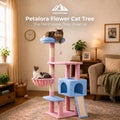 A pastel-colored cat tree in a cozy living room with two cats using it. The tree features pink and light blue carpeted platforms, scratching posts, a small hanging toy, a climbing ladder, and a small enclosed cubby.