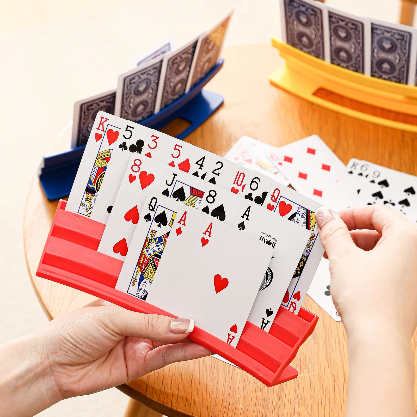 Playing Card Holder in red being used at a game table with blue and yellow holders behind it