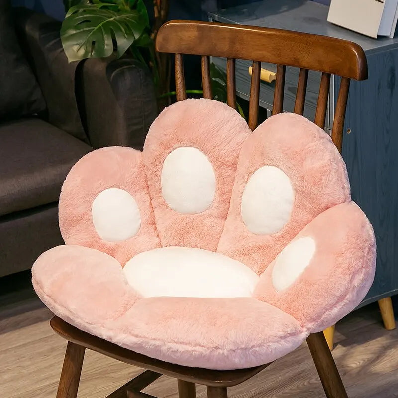 Plush Cat Paw Cushion in pink with white paw pads displayed on a wooden chair