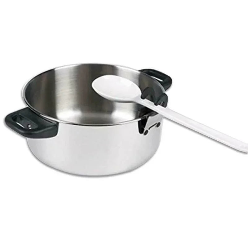 White cooking spoon resting in a black pot clip on the side of a stainless steel saucepan