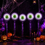 Purple Halloween Eyeball Balloons with green eyes and purple fringe arranged above pumpkins and cobwebs.