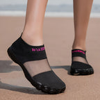 Quick-Dry Water Shoes black pair worn on sand with sheer instep panels and pink lettering.