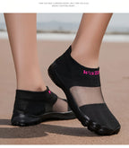Quick-Dry Water Shoes black pair on sand with one foot raised slightly to show the side profile.