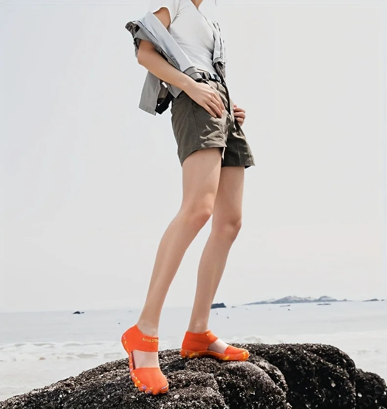 Quick-Dry Water Shoes orange pair worn by an adult standing on a rock beside the sea.