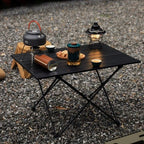 Roll-Up Camping Table black slatted table on gravel with a kettle, cups, snacks, and camping lantern.